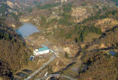 新潟県山古志村の東竹沢地区にできた天然ダム。青い屋根の建物の前に見える白い排水パイプで，ダム湖の水位を下げている（写真：国土交通省）